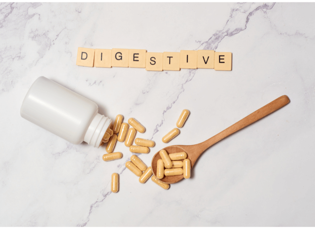 Cápsulas digestivas junto a frasco blanco y cuchara de madera sobre fondo claro con la palabra digestive formada con fichas de scrabble