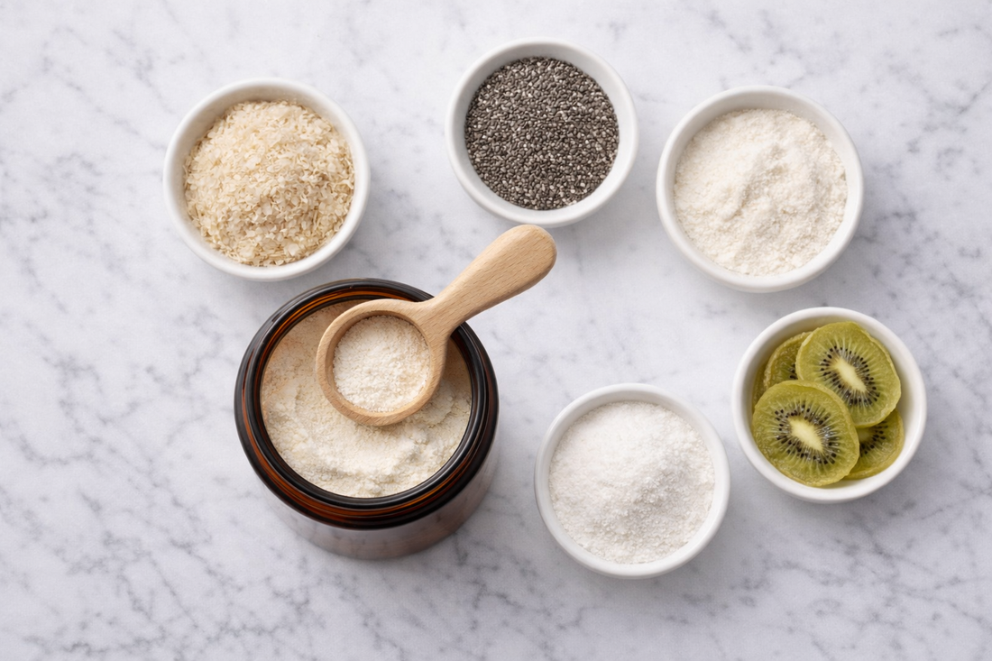 Suplemento de fibra en polvo abierto con cucharilla de madera, rodeado de psyllium, chía, linaza, inulina de achicoria y kiwi deshidratado: la combinación de fibra soluble, insoluble y prebiótica en una sola toma