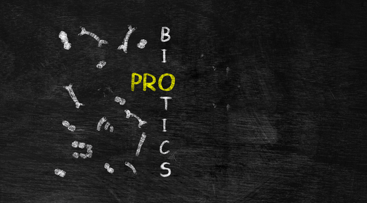 Palabra probiotics escrita en pizarra con tiza, destacando en amarillo la sílaba PRO, rodeada de ilustraciones de bacterias