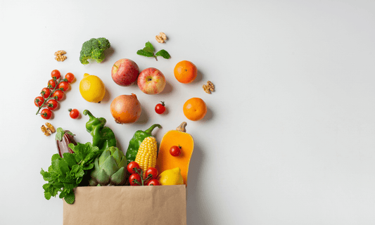 Bolsa de mercado con frutas y verduras frescas como manzanas, cebolla, calabaza, maíz, brócoli y tomates, ideales para una alimentación saludable y rica en fibra